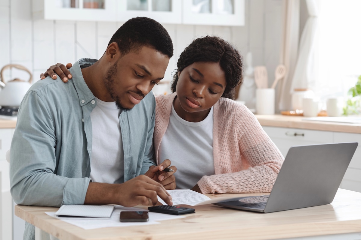 Homebuyer couple reviewing documents on a laptop at a kitchen table
